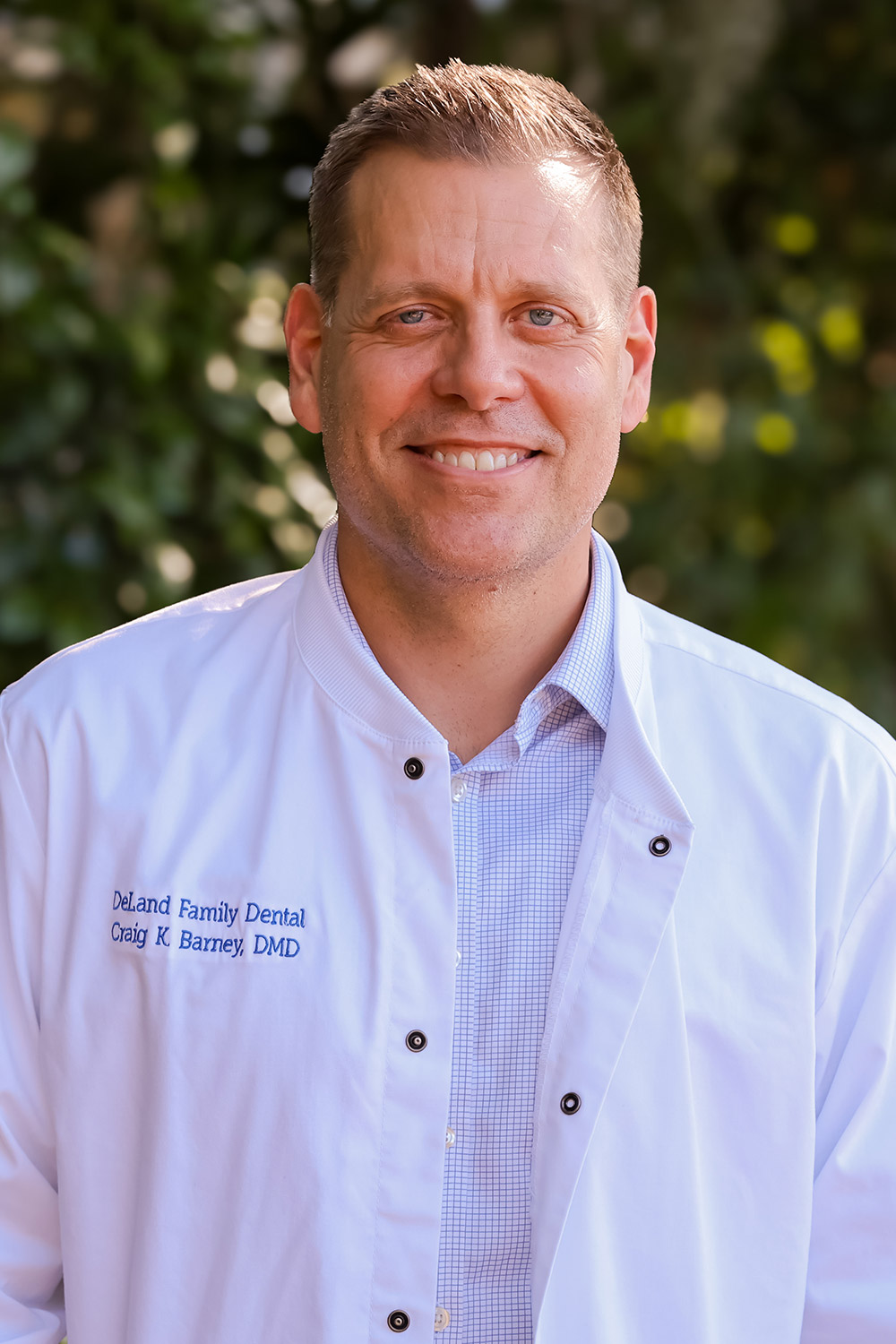 Dr. Craig Barney, DMD of DeLand Family Dental, smiling outdoors in a white dental coat.