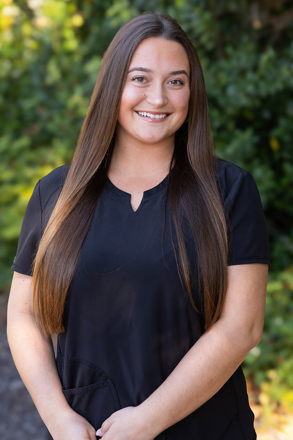 Jenna, Dental Assistant at DeLand Family Dental, smiling outdoors in black scrubs.